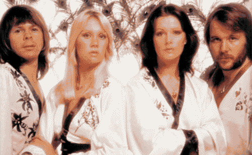 A photo of Swedish dance pop group, ABBA. They are wearing white kimonos with black floral accents standing in front of a background filled with peacock feathers.